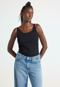 Sort ærmeløs top med en runde halsudskæring, parret med lyseblå højtaljede denimjeans, præsenteret mod en neutral baggrund.