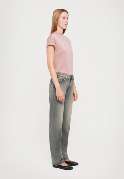 Top corto de manga corta color rosa claro combinado con jeans de tiro alto grises y zapatos planos negros. Los jeans tienen un diseño desgastado. Vista lateral del conjunto.