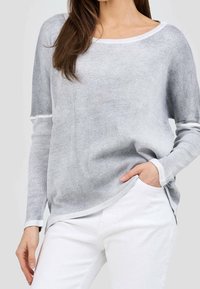 Ljust grå långärmad topp med ribbat mönster, breda axelremmar, kontrasterande vitt kant och sidofickor, tillsammans med vita byxor.