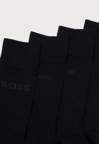Meias pretas em um pacote, feitas de tecido suave. Apresentam um punho canelado e uma marcação discreta "BOSS" em preto mais claro na lateral.