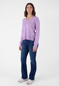 Maglione lilla a V con maniche lunghe, orlo a coste, abbinato a jeans a zampa blu e sneakers bianche. Design semplice, texture liscia.