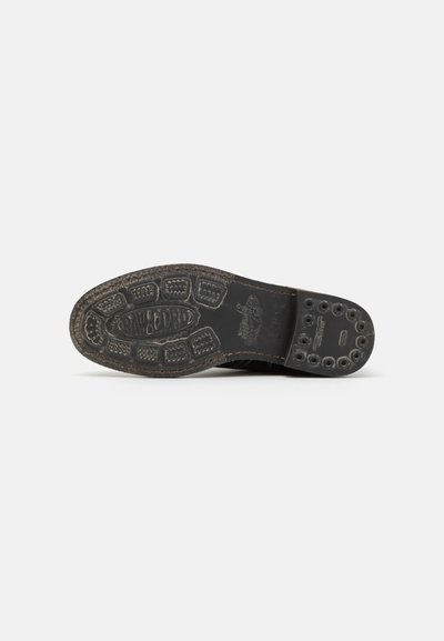 Sole di scarpa in gomma nera con pattern testurizzato, caratterizzata da battistrada circolari e rettangolari. Logo inciso e fori di drenaggio visibili.