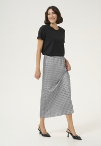 Camiseta negra de manga corta combinada con una falda maxi gris con lunares. La falda tiene una textura satinada suave y llega hasta el tobillo. Zapatos de tacón negros.