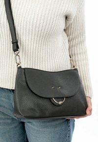 Borsa a tracolla in pelle nera con finitura texturizzata, chiusura a patta rotonda e un accento in anello argentato. Cinghia regolabile inclusa.