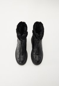 Des bottes noires à la cheville présentent un extérieur en cuir rembourré, un col en fausse fourrure et une fermeture éclair à l'avant. La semelle est texturée pour une meilleure adhérence.