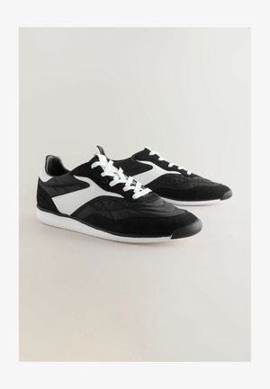 Black and white athletic shoes with a combination of leather and suede, featuring a textured design, round toe, and white laces.