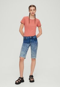 Korte mouwen roze t-shirt gecombineerd met blauwe denim shorts met een licht- naar donkergradiënt, aangevuld met zwarte sandalen.