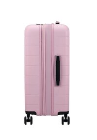 Valise rose rigide avec des rainures verticales, fermetures éclair noires et une poignée noire. Elle dispose de quatre roues pivotantes noires pour une mobilité facile.