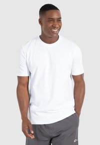 Hvid crew-neck t-shirt lavet af bomuld, med kortærmer og en afslappet pasform, parret med grå shorts. Model står med hænderne i lommerne.