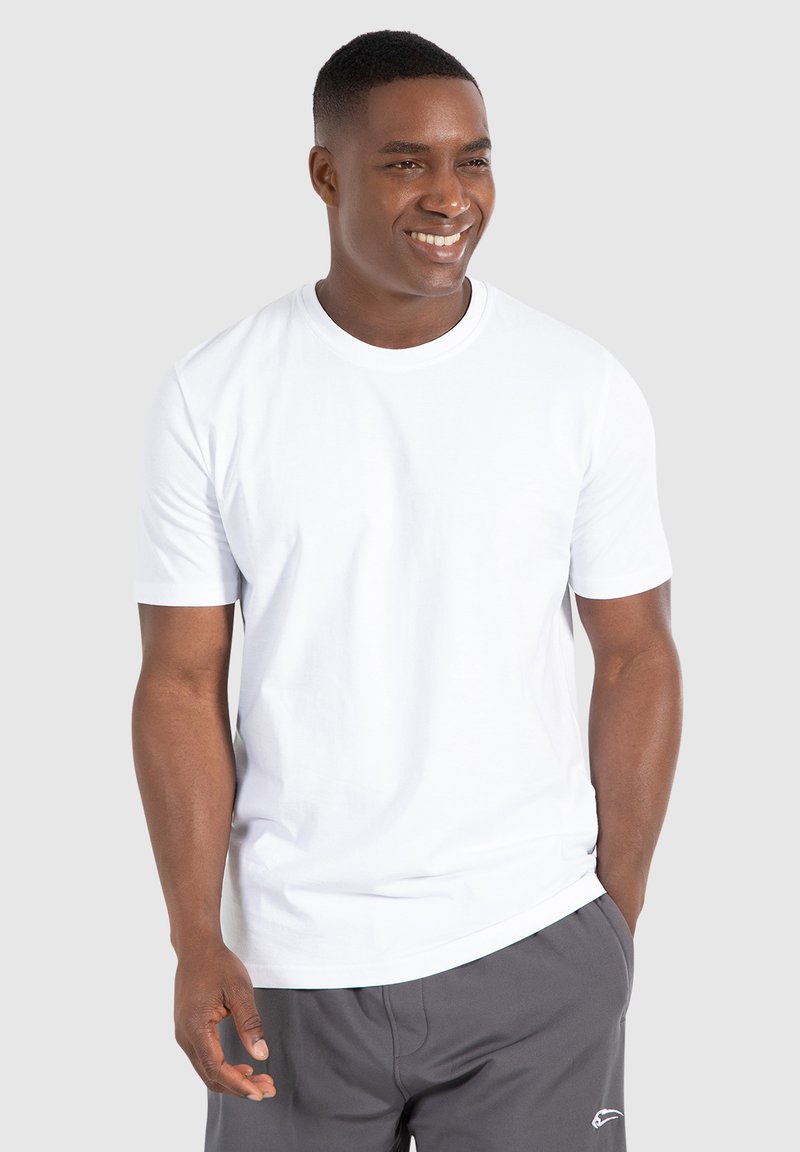 Hvid crew-neck t-shirt lavet af bomuld, med kortærmer og en afslappet pasform, parret med grå shorts. Model står med hænderne i lommerne.