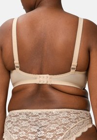 Béžová podprsenka s nastavitelnými ramínky, s hladkým povrchem a zapínáním na háček a oko. Krajkový lem dodává detail na okrajích.