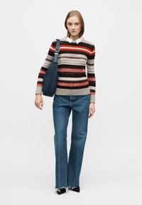 Striped sweater in beige, red, and brown, paired with blue flared jeans featuring frayed hems. Dark blue shoulder bag, black pointed shoes.