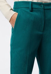 Teal green trousers with a smooth texture, featuring a high waistband, button closure, and side pockets. Cut with a tailored silhouette.