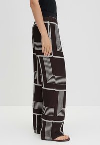 Zwarte wijde pantalons met een geometrisch wit patroon, in een losse pasvorm en met een elastische tailleband, gemaakt van lichtgewicht stof.