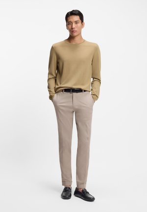 Maglione beige a maniche lunghe, pantaloni beige chiaro, cintura nera e mocassini neri. Il tessuto appare liscio con un design aderente.