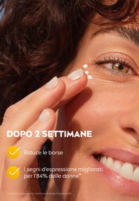 Crema idratante applicata sotto l'occhio con una texture liscia. Primo piano di un occhio di donna, con un incarnato chiaro e capelli scuri e ricci.