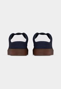 Paire de baskets bleu marine avec panneaux de talon blancs et semelles marron vues de dos sur un fond uni.