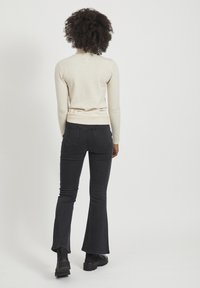 Crème kleurige sweater met lange mouwen, gecombineerd met zwarte flare jeans en enkellaarsjes. De jeans hebben twee achterzakken en een gladde textuur.