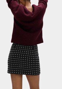 Burgunderfarbener, oversized Pullover aus weichem Stoff, kombiniert mit einem engen schwarzen Rock mit einem weißen Karomuster und Kreuzmustern.