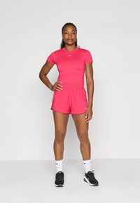 Tutu de sport roz, format dintr-o bluză scurtă, ajustată, cu mânecă scurtă și pantaloni scurți asortați, ambele realizate dintr-un material neted și elastic.