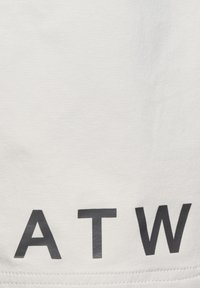 Vit tyg med en slät yta som har djärva, svarta versaler "A T W" tryckta framträdande. Enkel, modern design.