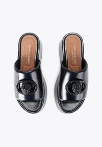 Sandales en cuir noir à enfiler avec une sangle incurvée, dotées d'une boucle métallique décorative et d'une semelle intérieure texturée. Semelle plate-forme légère.