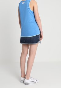 Blå ärmlös linne med rund halsringning, tillsammans med en jeanskjol med rak skärning och vita sneakers.