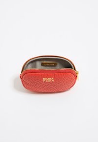 Bolso de cuero texturizado rojo con forma redondeada, hardware dorado y cierre de cremallera. El interior presenta un forro claro en contraste.