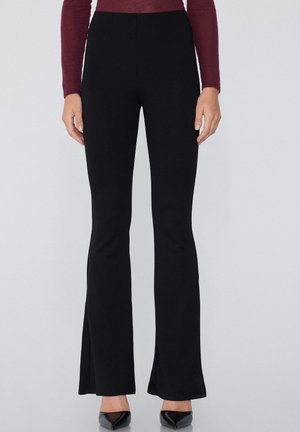 Pantalones acampanados negros con cintura alta, hechos de una tela elástica. Presentan una textura suave y una silueta ajustada hasta la rodilla.