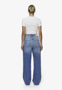 Vide ben denim jeans i lyseblå, høyt liv med fem lommer, falmet tekstur på beina, kombinert med en hvit tettsittende crop top.