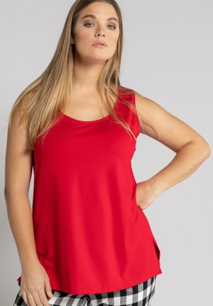 Rotes ärmelloses Oberteil mit rundem Halsausschnitt, aus glattem Stoff gefertigt. Mit seitlichen Schlitzen, kombiniert mit schwarz-weißen karierten Hosen.