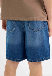 Shorts de mezclilla con un lavado azul desvanecido, diseño de cinco bolsillos y detalles de costura. Tienen un ajuste relajado y terminan justo por encima de la rodilla.