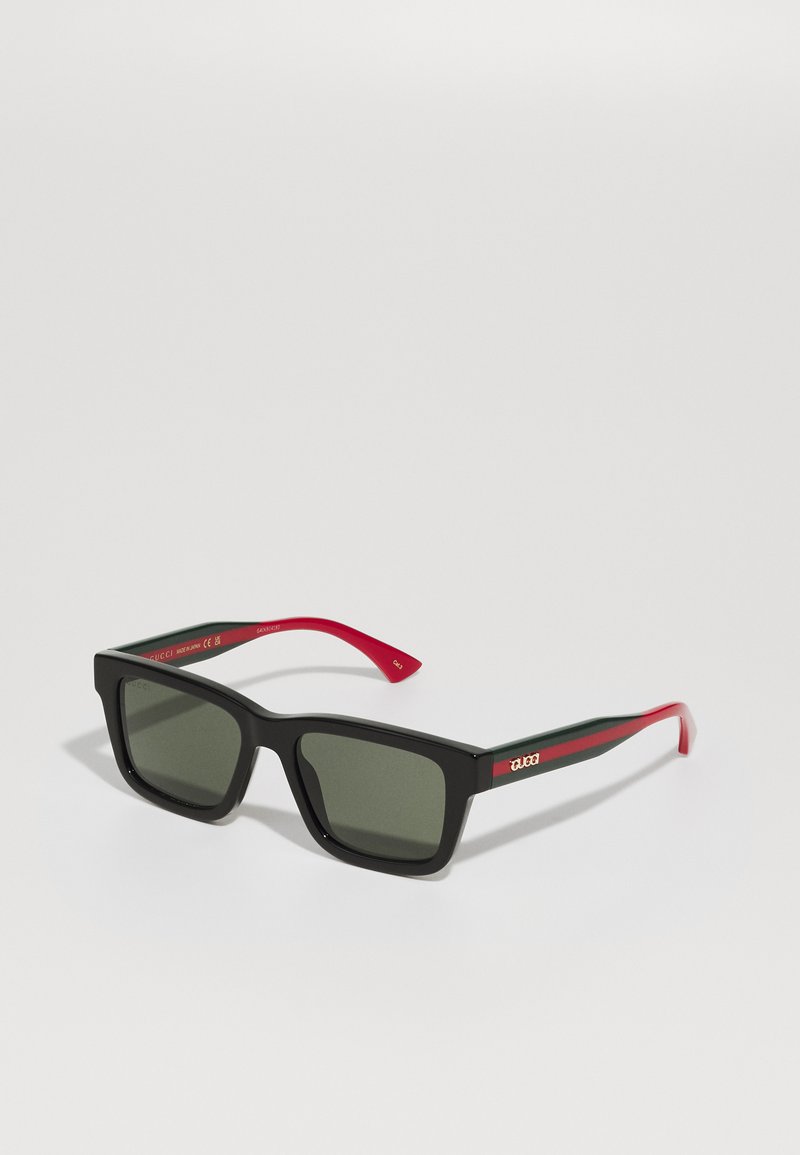 Ochelari de soare negri, în formă rectangulară, cu lentile gri, brațe cu dungi roșii și verzi, și un logo auriu pe tâmplă. Finisaj mat și design îndrăzneț.