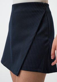 Gonna blu navy con righe bianche, caratterizzata da un design avvolgente diagonale. Realizzata in un tessuto morbido con una leggera lucentezza e con una cerniera laterale.