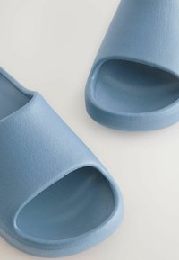 Lyseblå hæl-sandaler lavet af tekstureret gummi. Åben tå-design med en glat overdel og en let forhøjet hæl.