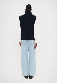 Gilet en polaire marine avec col haut, associé à un jean large bleu clair et des chaussures noires. Texture lisse ; design simple et fonctionnel.