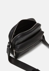 Borsa a tracolla nera in pelle con foderatura grigia a contrasto, scomparti con zip e dettagli del logo. Include una robusta tracolla regolabile.
