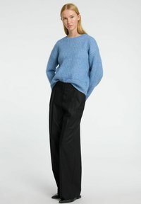 Lyst blå strikket sweater med et struktureret mønster, parret med sorte, løse bukser med vidde, som har en afslappet pasform og rund halsudskæring.
