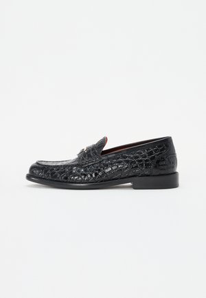 Sorte læder loafers med krokodille tekstur, flad hæl, rund tå og dekorativ rem over vangen. Poleret finish og minimale accenter.
