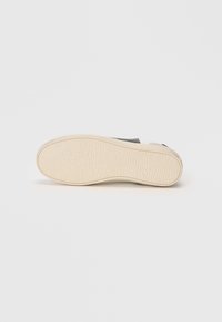 Suola di sneaker, in gomma, testurizzata, beige, con una superficie battistrada a motivo. Presenta una parte superiore nera in contrasto, progettata per un grip ottimale.