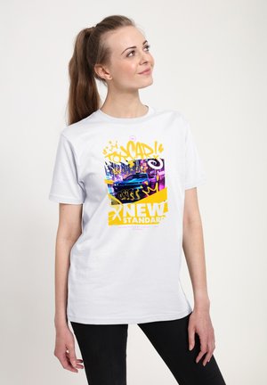 Ung kvinde med hestehale iført en hvid t-shirt med neon bylandskab og gul graffiti tekst, "New Standard" og "Drift."
