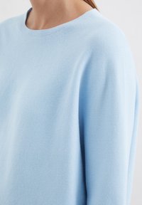 Pull bleu clair avec un motif tricoté texturé, encolure ronde et coupe légèrement ample. Les coutures sont visibles le long des bords.