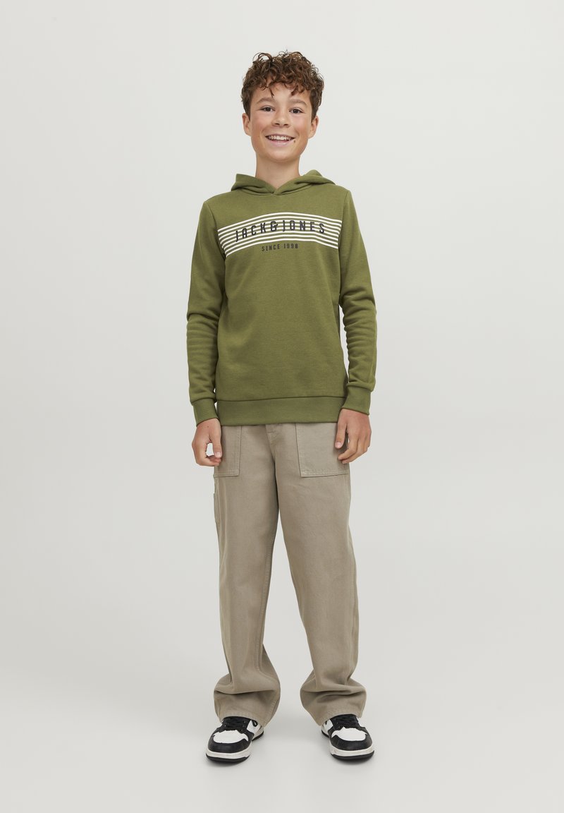 Sudadera verde con capucha y diseño de rayas blancas con texto, combinada con pantalones cargo beige y zapatillas negras y blancas. Un look simple y casual.