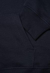 Felpa blu navy con polsini a costine e tasca a marsupio. Presenta una superficie liscia e dettagli di cucitura visibili lungo i bordi.