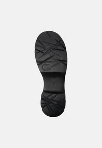 Suola di scarpa in gomma nera con un pattern testurizzato caratterizzato da linee diagonali e scanalature per una migliore aderenza. Presenta un marchio sulla superficie.