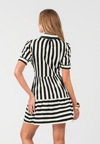 Abito a righe bianche e nere con maniche corte, un corpetto aderente e una gonna ampia. Presenta un colletto e un design con orlo a strati.