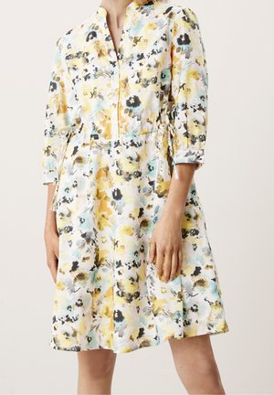 Vestido blanco con estampado floral en amarillo, negro y azul, mangas tres cuartos y lazos laterales en la cintura.