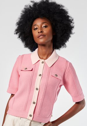 Cardigan a maniche corte di un delicato rosa, con un colletto crema a contrasto, due tasche frontali e bottoni rotondi, caratterizzato da un motivo a maglia testurizzato.