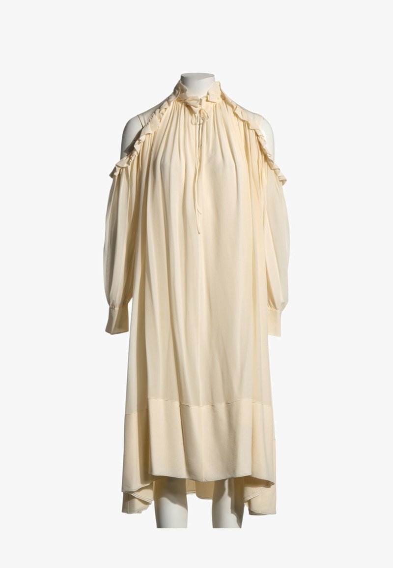 Robe de couleur crème à manches longues avec découpes volantées aux épaules dénudées et col montant froncé avec un lien à l'avant.