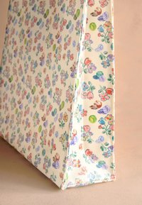 Obdĺžniková béžová taška na rameno s farebnými malými kvetinovými a listovými vzormi v ružovej, fialovej, zelenej a modrej na neutrálnom pozadí.